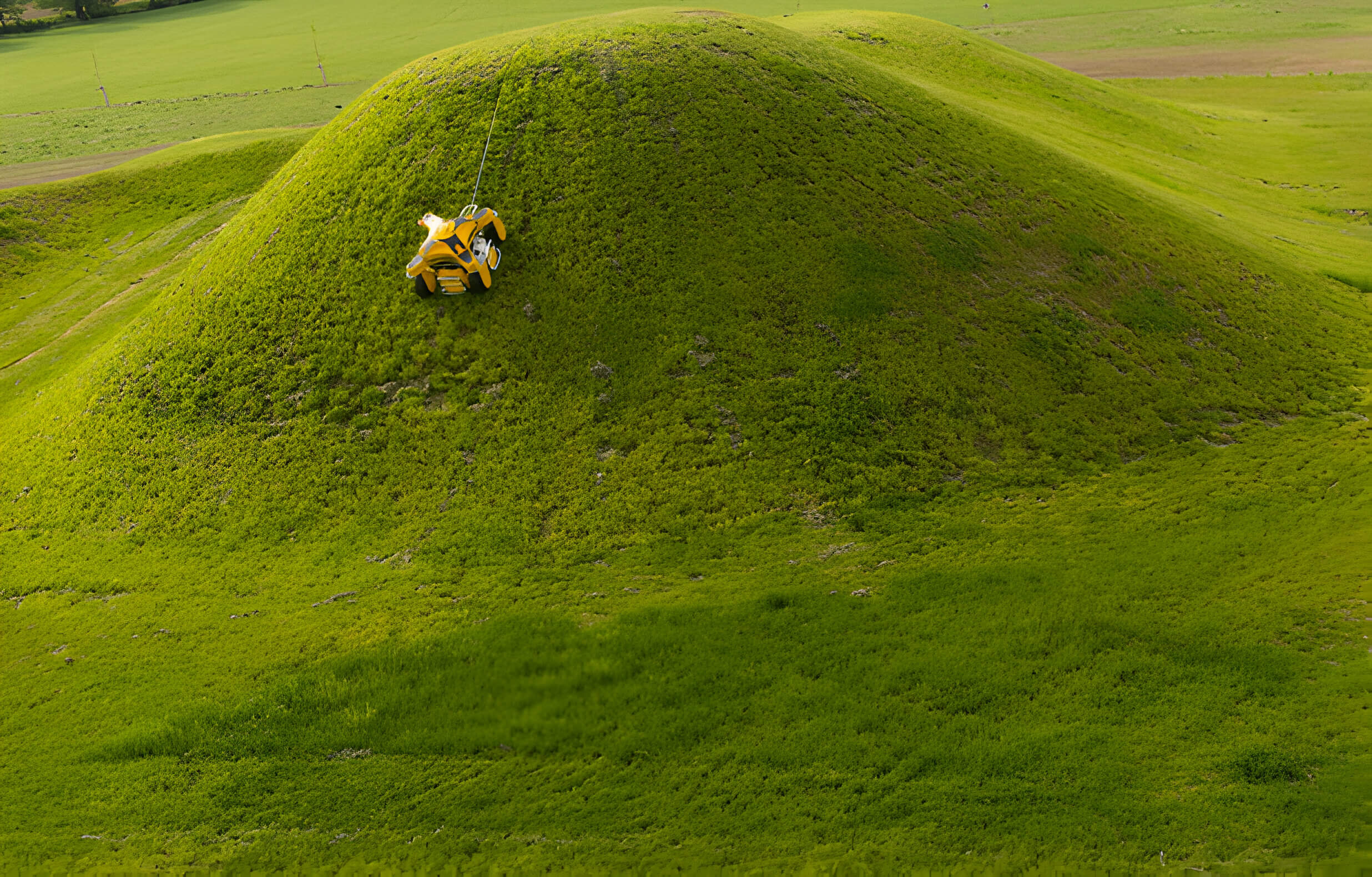 An aerial view of a SPIDER mower on a lush green hill, highlighting its ability to navigate challenging landscapes.