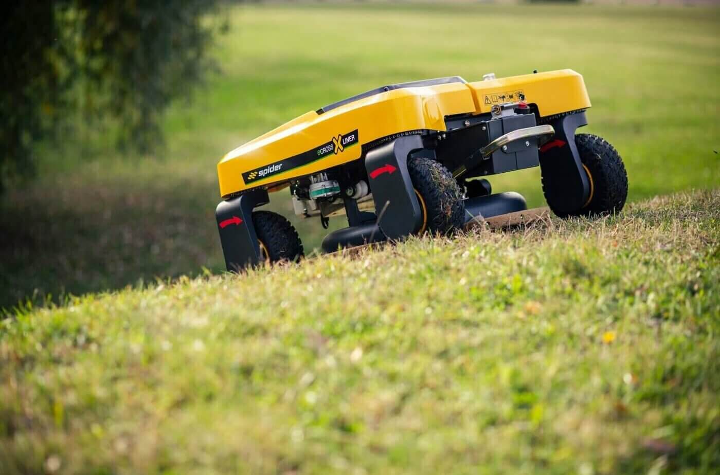 A yellow and black SPIDER eCROSSLINER mower on a grassy slope, showcasing its compact design and terrain versatility.